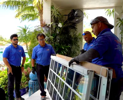 Team in blue shirts installing large glass panel near tropical building
